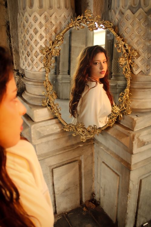 Free An elegant woman in white stands before a vintage mirror, reflecting historical architecture. Stock Photo