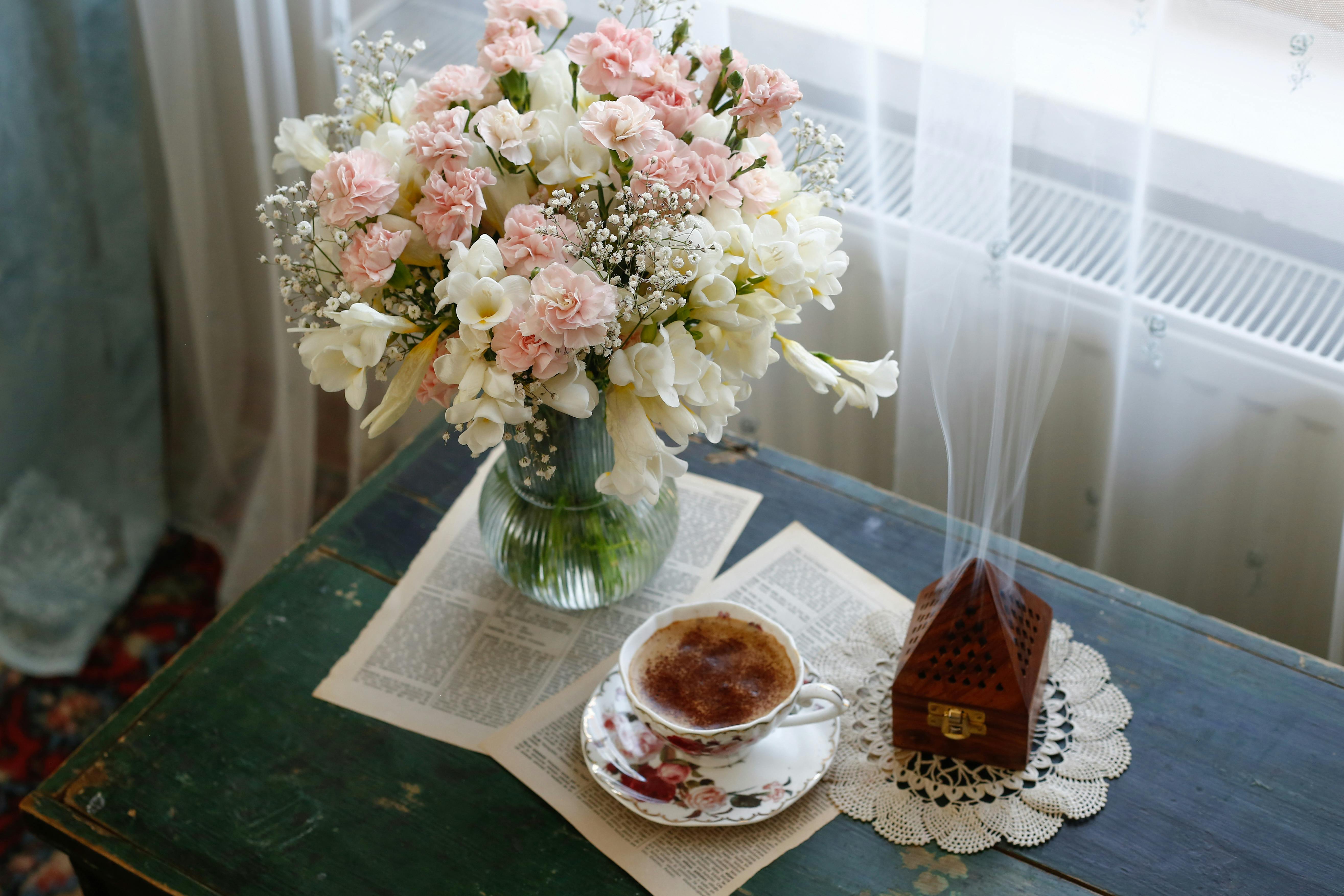 A serene setting with a floral bouquet, steaming tea, and incense on a wooden table.