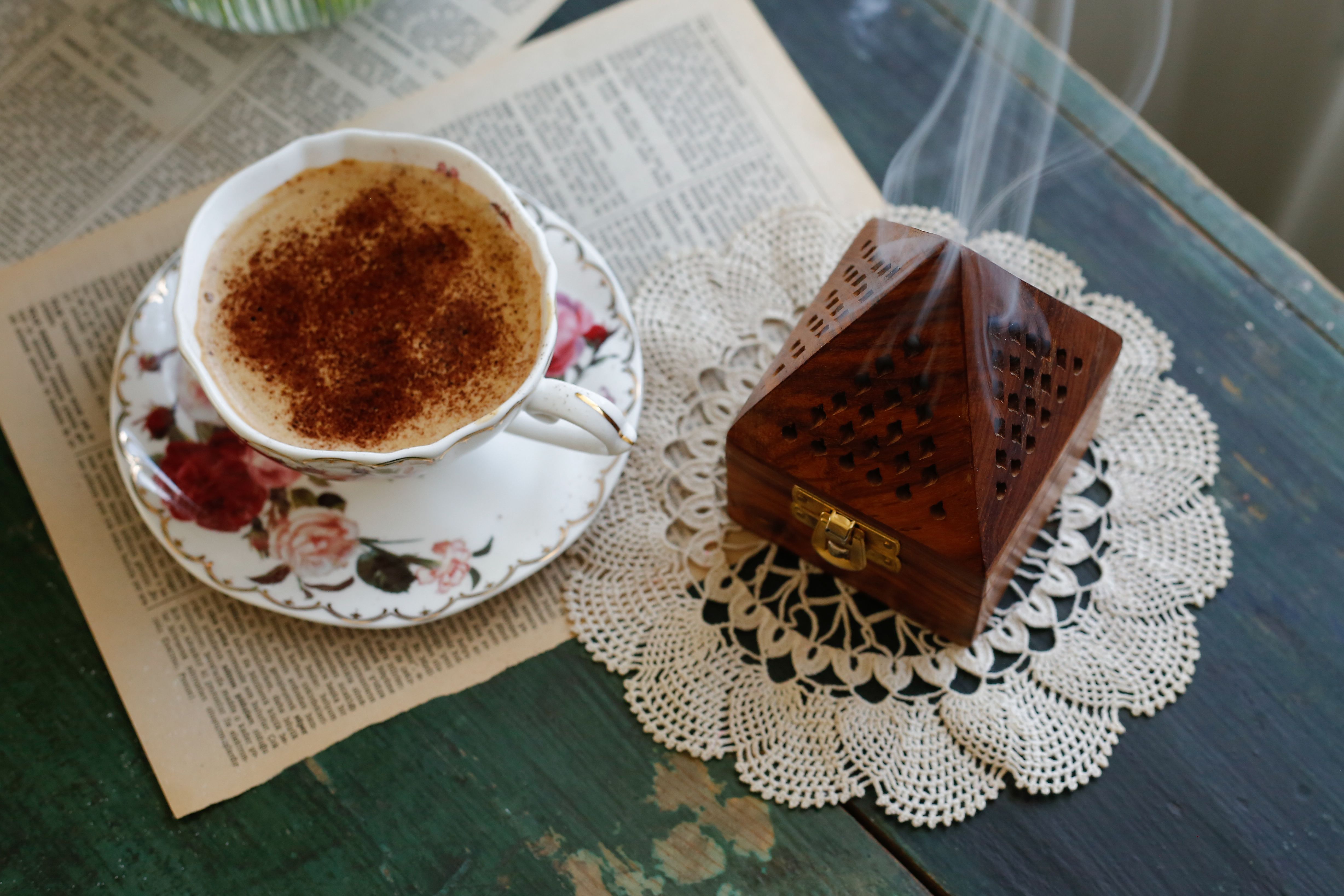 Warm still life of a coffee cup and a wooden incense box on a crochet doily.