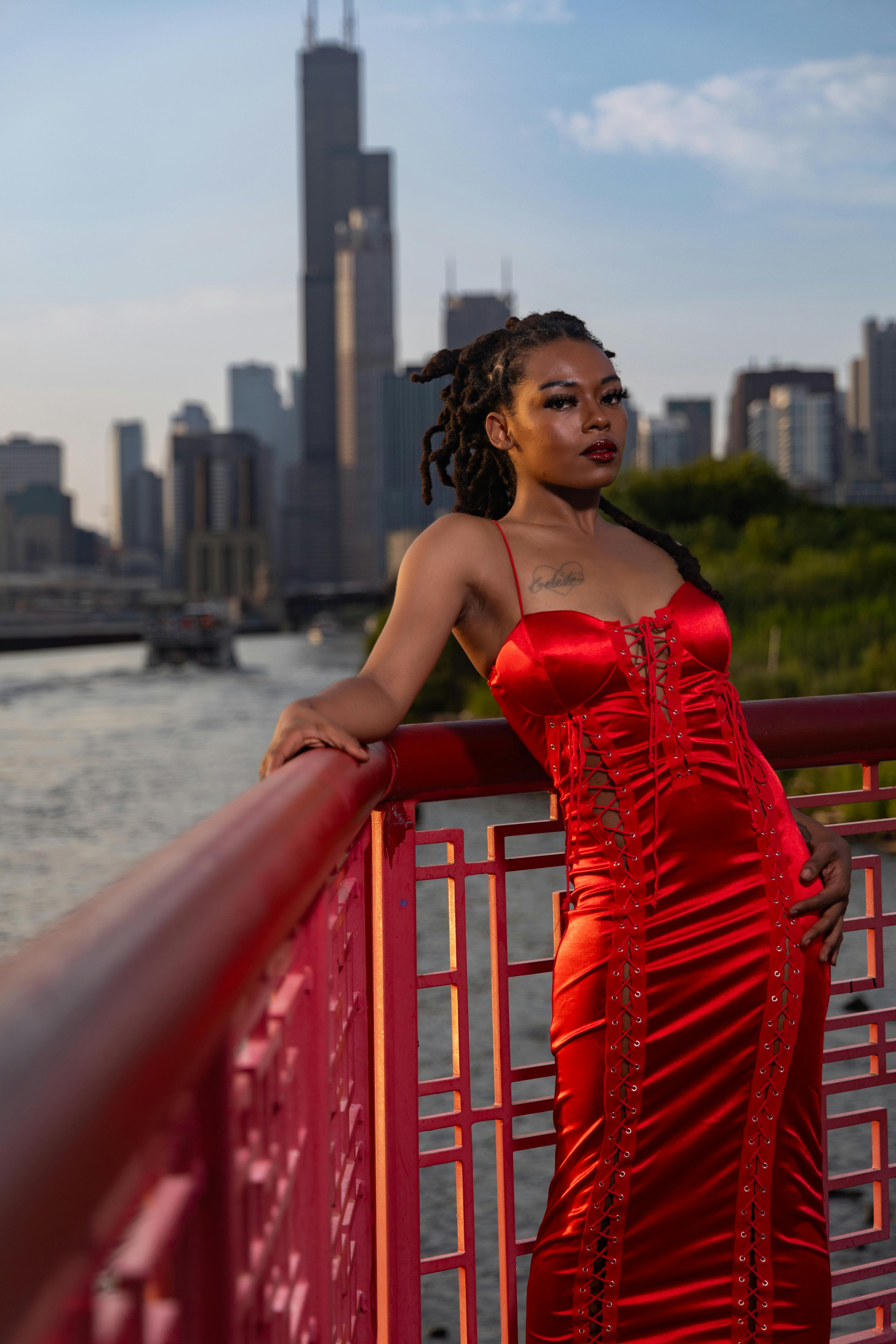 Elegant fashion model poses by Chicago River with skyline view.