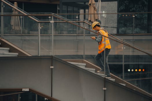 An adult construction worker in a hard hat and vest ascending stairs inside a building.