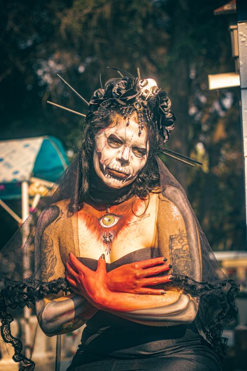 Free Woman in Day of the Dead costume with ornate headdress and skull makeup in vibrant outdoor setting. Stock Photo