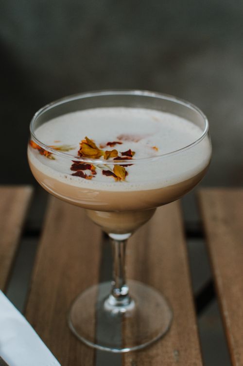 Free A creamy latte topped with dried marigold petals, served on a rustic wooden table in natural light. Stock Photo