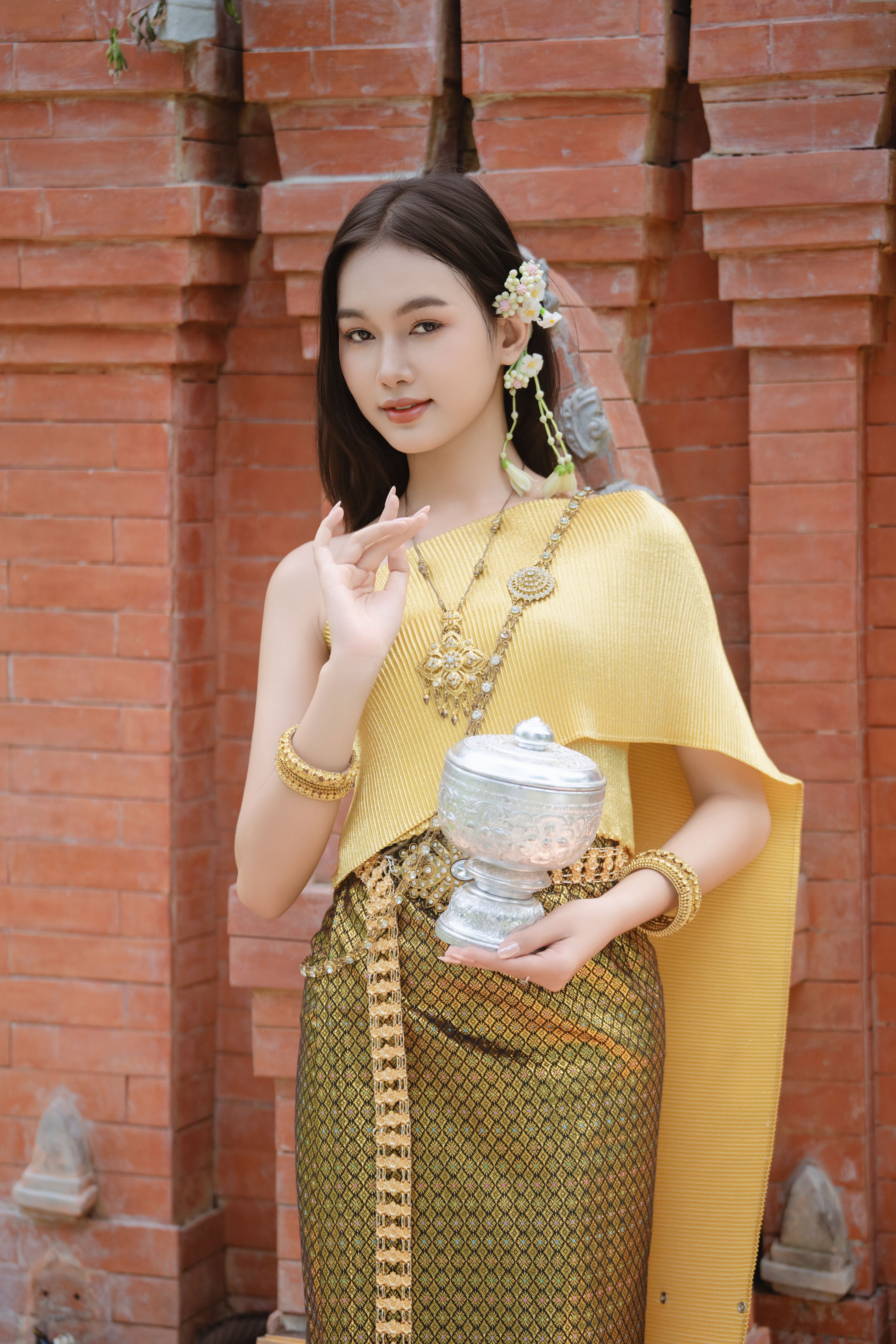 Woman in elegant, traditional Asian attire holding an ornate silver urn.