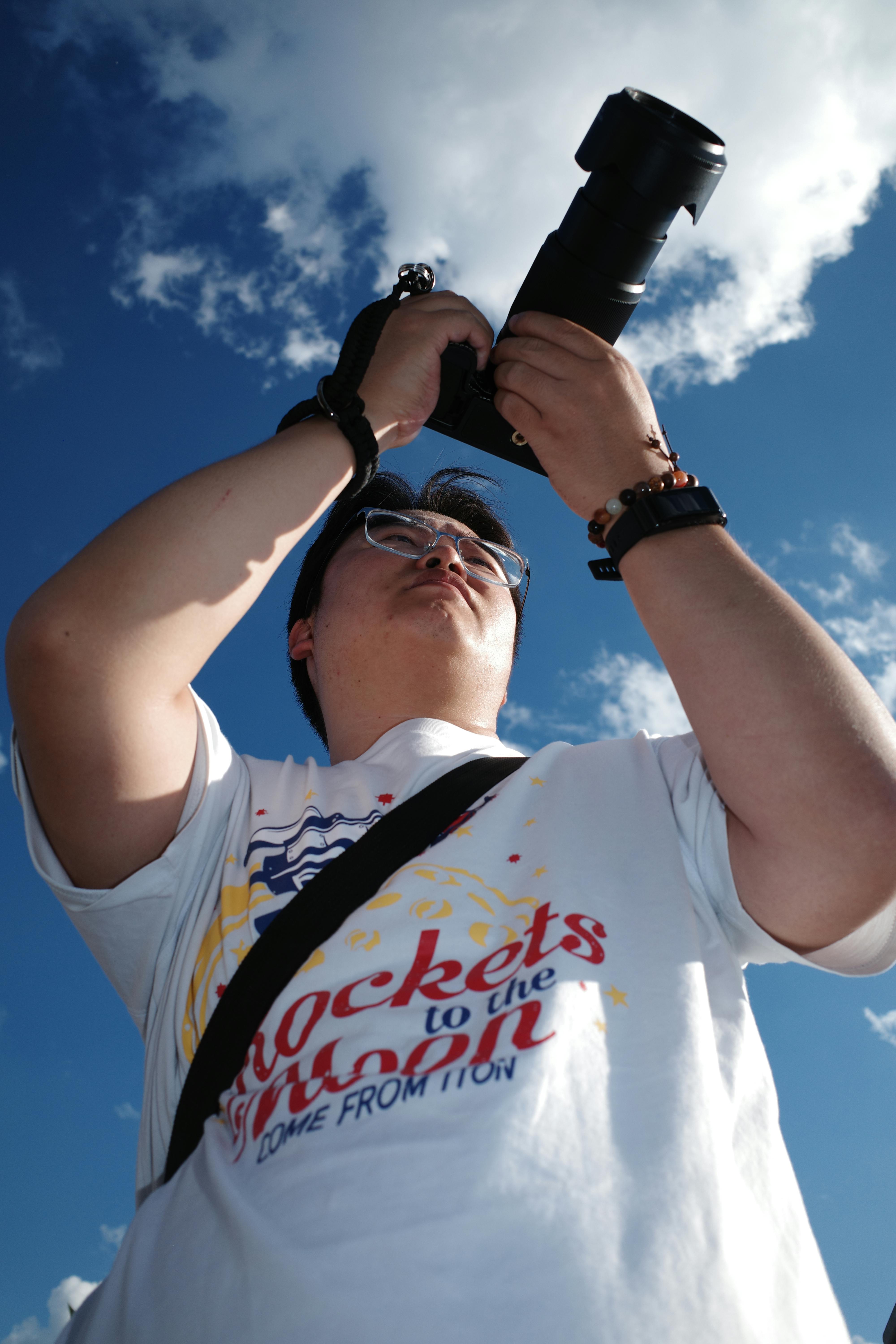 A focused photographer captures a sky view using a large camera lens outdoors.