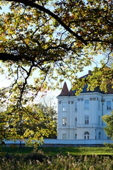 A grand white mansion surrounded by vibrant autumn leaves under a clear blue sky.