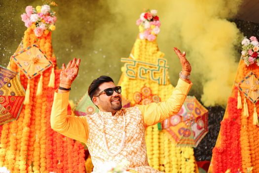 Joyful Indian groom at a vibrant Haldi ceremony with floral decorations and traditional attire.