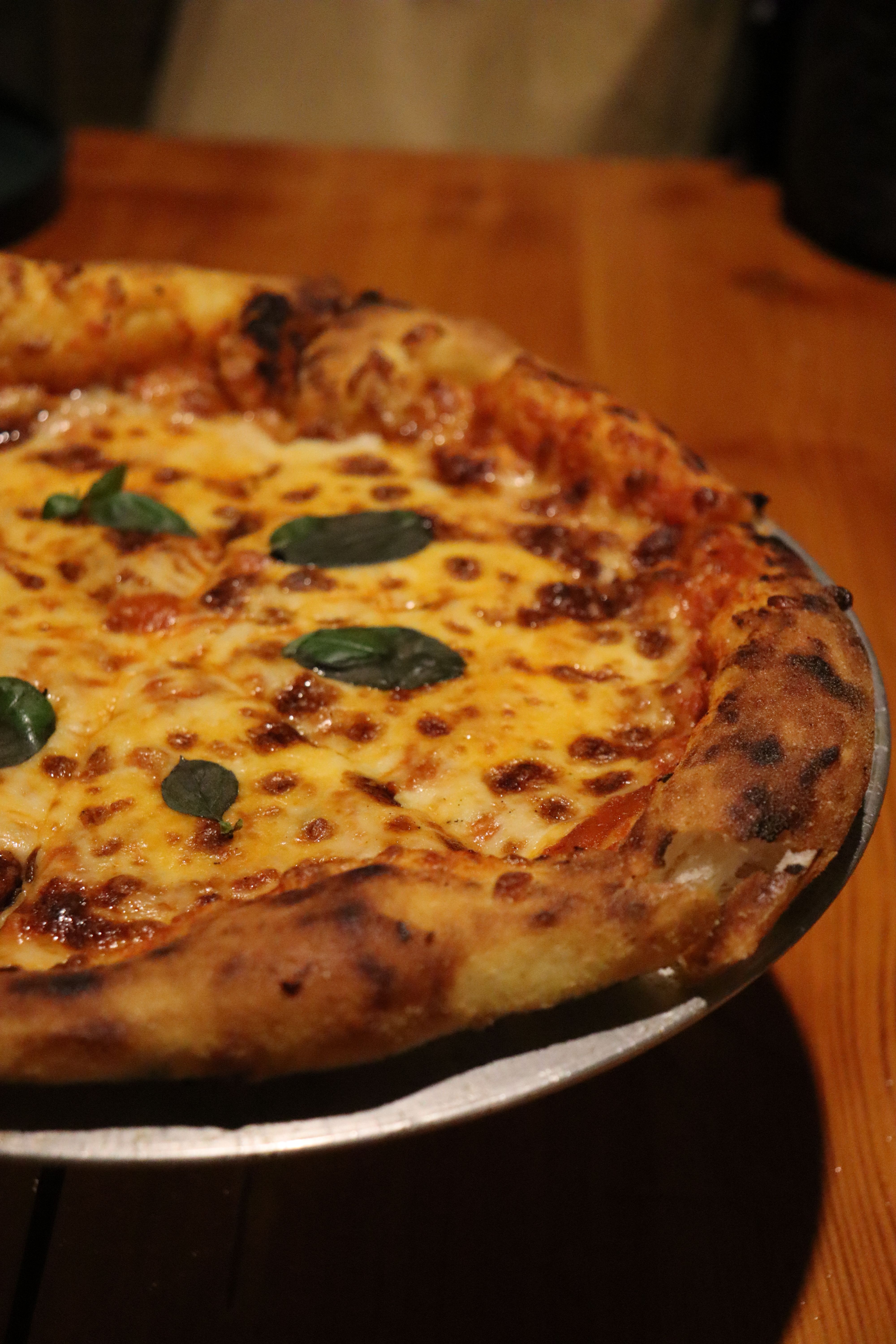 Close-up of a freshly baked Margherita pizza with basil garnish on a wooden table.