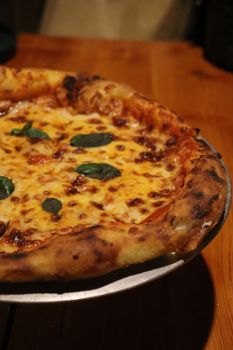 Close-up of a freshly baked Margherita pizza with basil garnish on a wooden table.