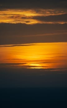 Beautiful golden sunset over a vast ocean horizon with layered clouds in a dramatic evening sky.