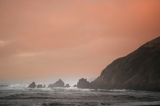 A serene coastal landscape featuring dramatic rocks under a vivid sunset sky.