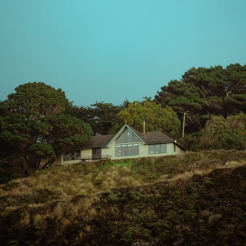 Free A solitary house surrounded by dense trees and green hills under a clear blue sky. Stock Photo