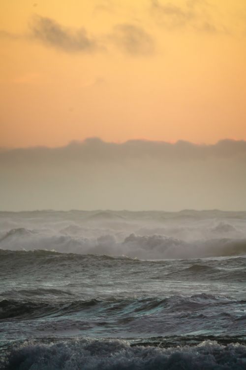Free Vibrant ocean waves roll under a warm sunrise, creating a dramatic seascape. Stock Photo