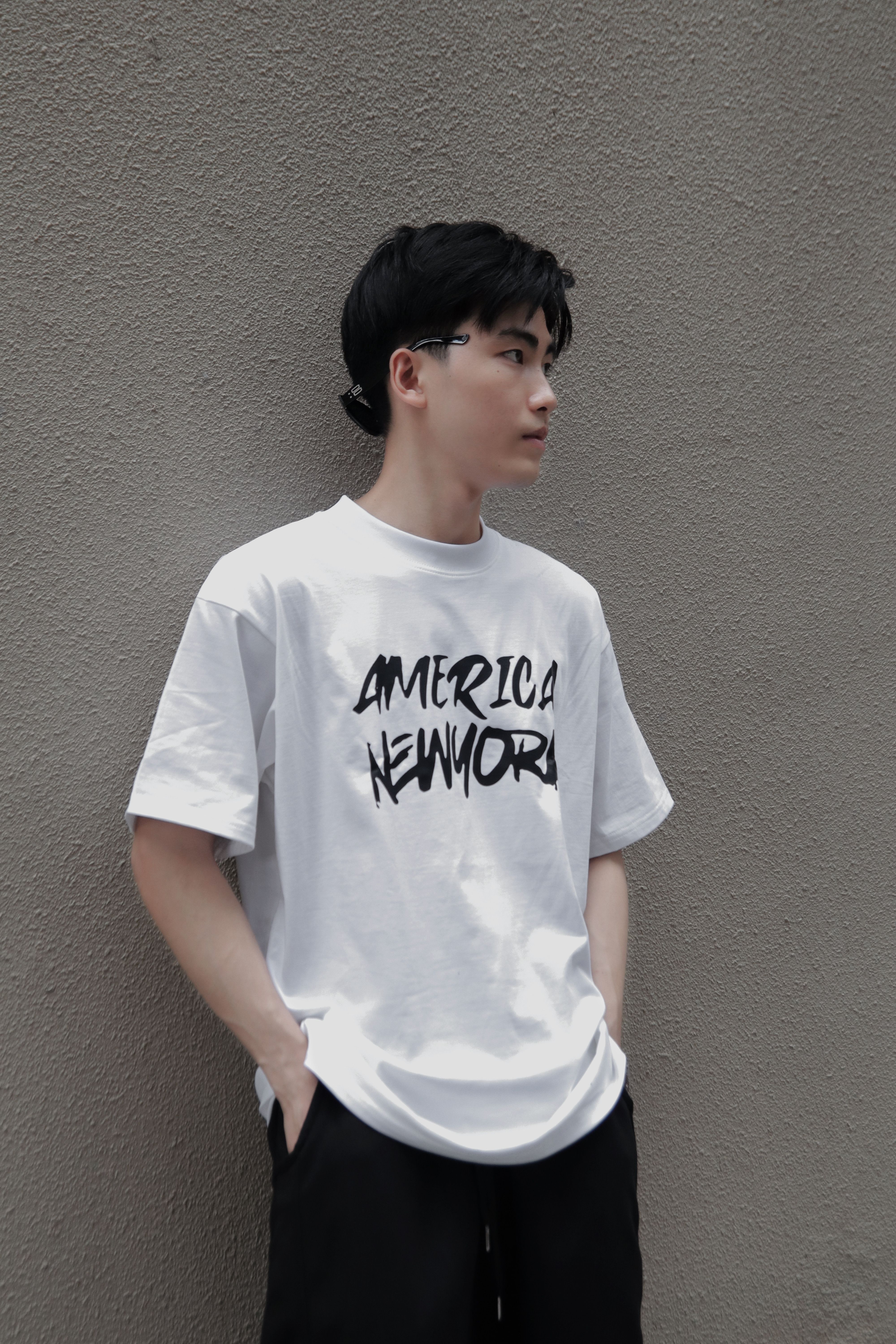 Casual portrait of a young man in a New York t-shirt leaning on a textured wall.