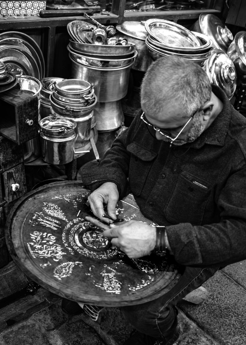 A skilled coppersmith engraving intricate designs on copperware at Gaziantep bazaar.