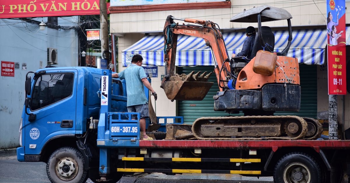Excavator being loaded onto a truck in a busy urban street, showcasing construction work.