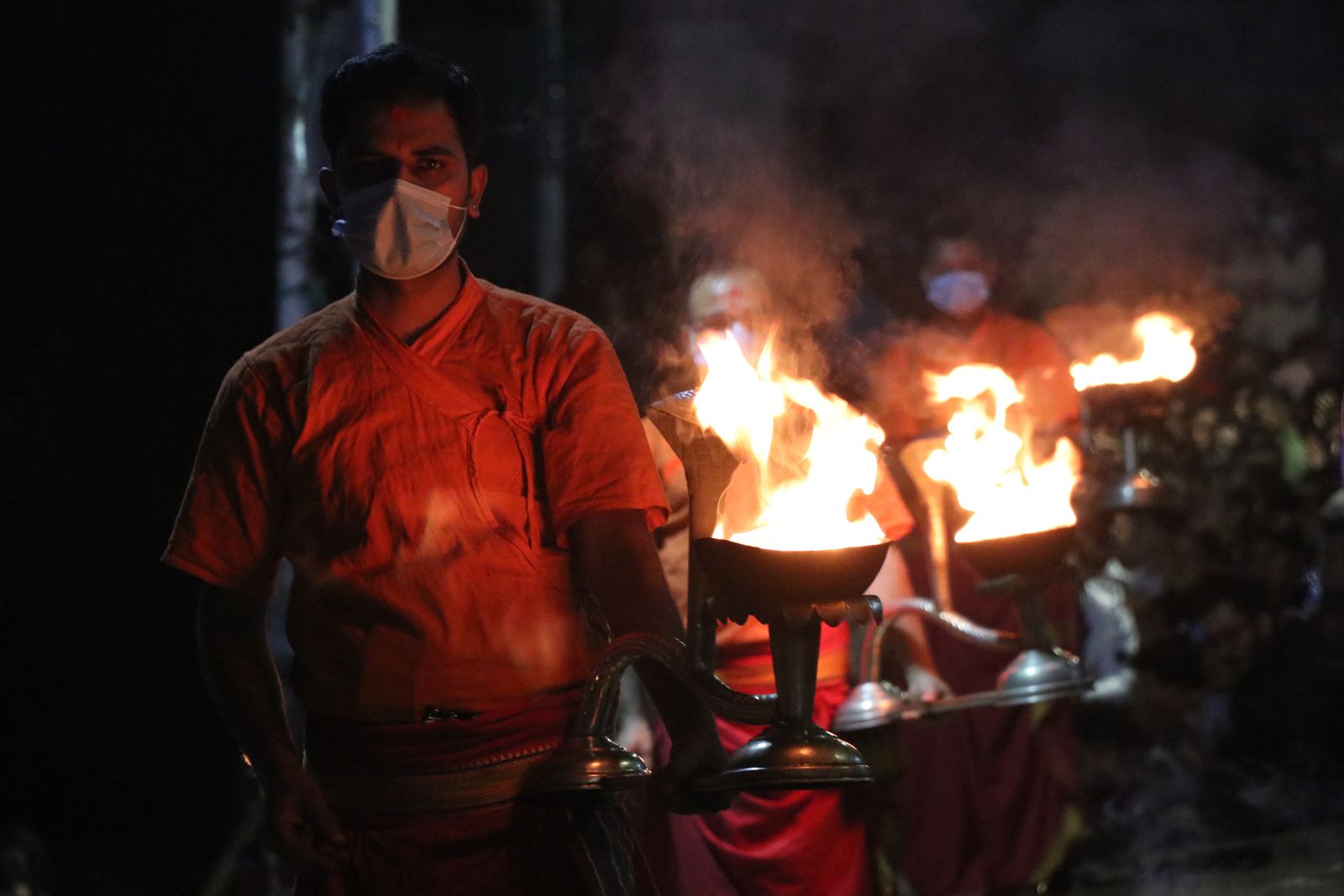 Priests in orange raise flaming brass lamps during the evening aarti at Pashupatinath, Kathmandu