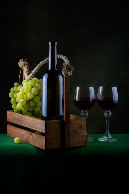 A dark-styled wine display with red wine glasses and green grapes in a wooden crate.