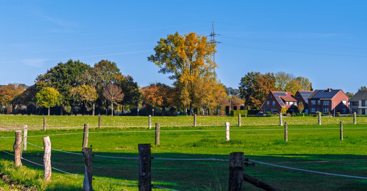 Scenic view of a rural landscape featuring green fields, trees in autumn colors, and distant houses.