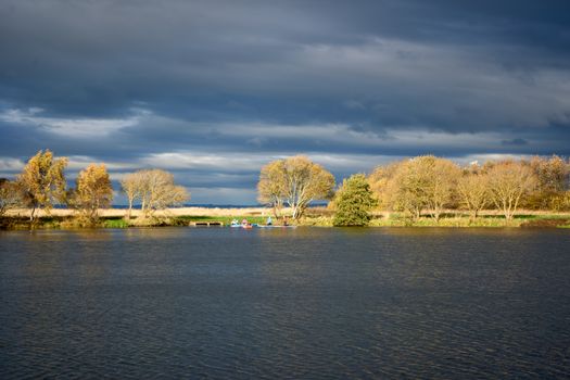 Peaceful autumn scene with trees and dramatic clouds by a calm river.
