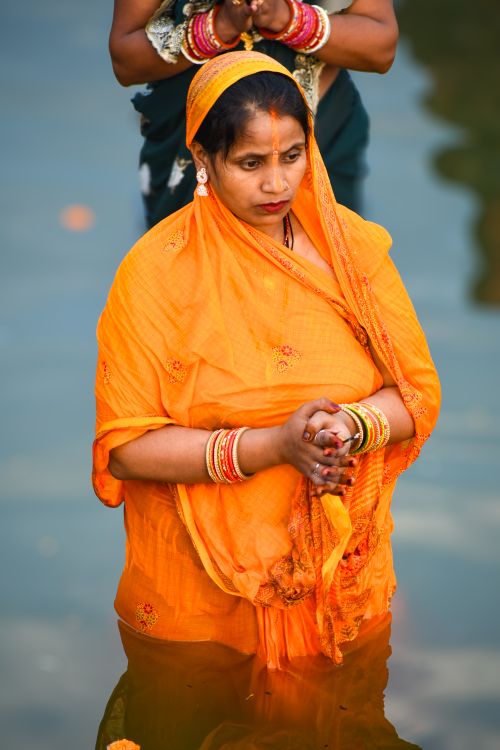 Free An adult female in vibrant orange saree participates in water ritual during a cultural ceremony. Stock Photo