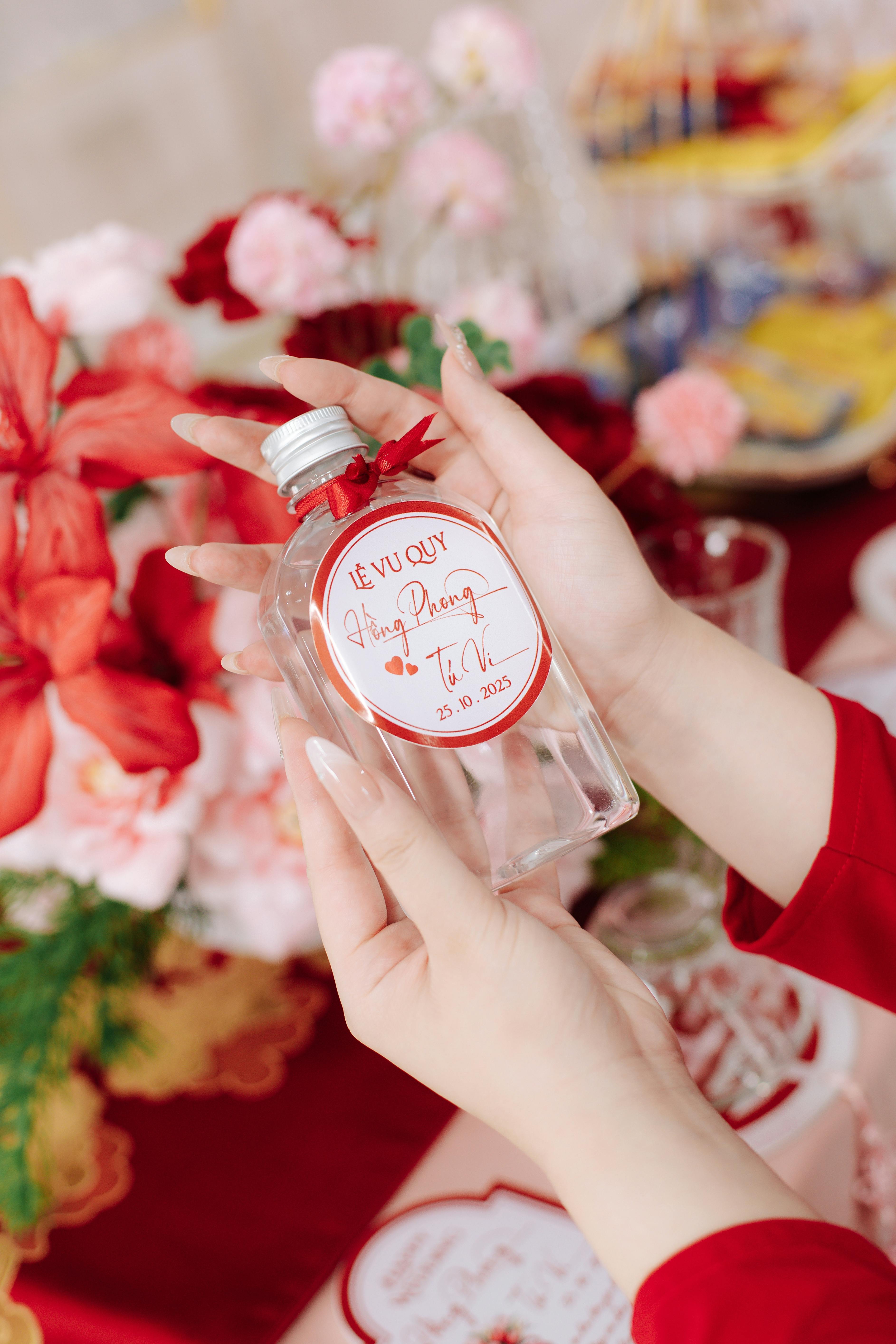 Close-up of hands holding a wedding favor bottle amidst vibrant flowers.