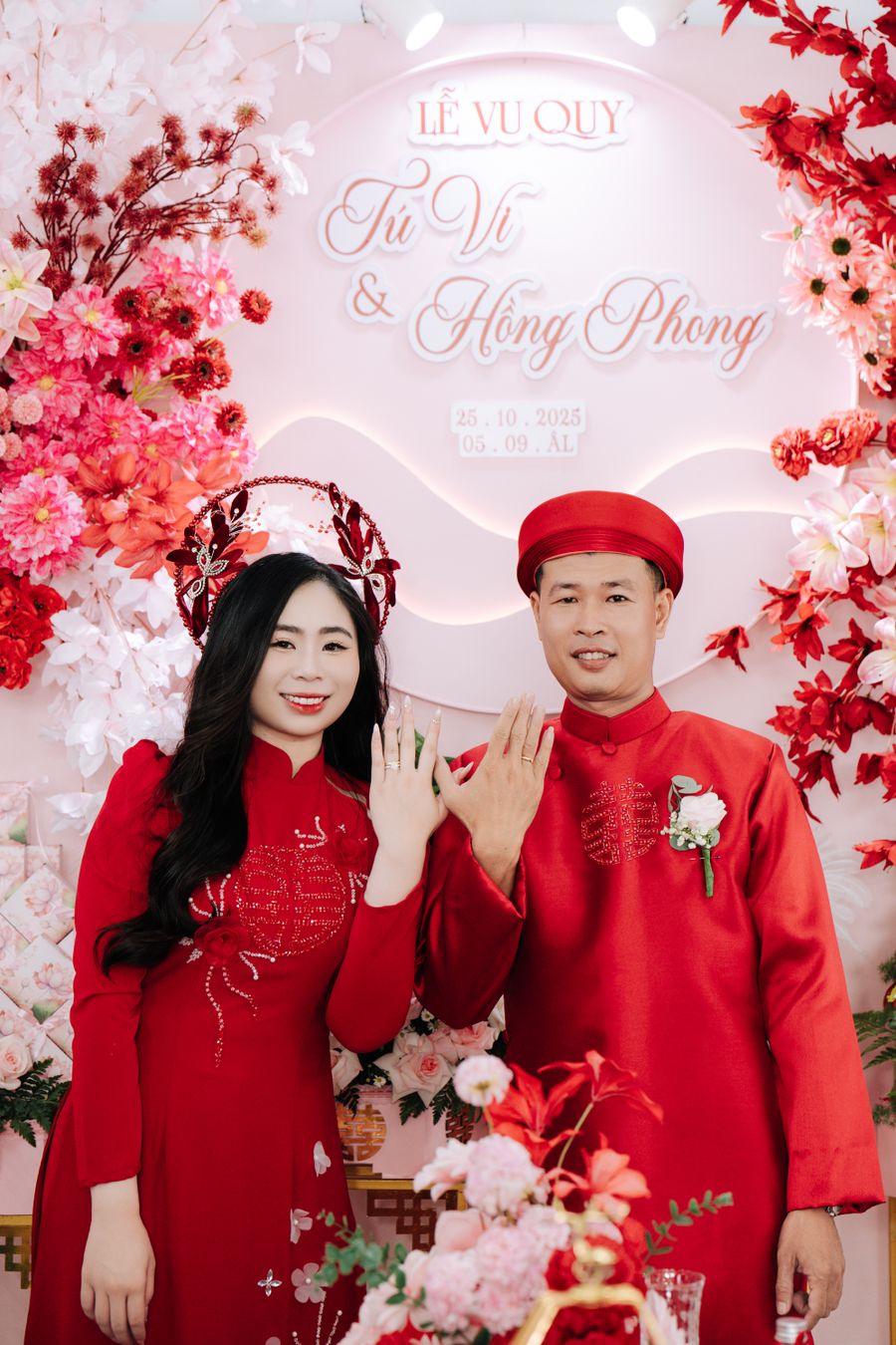 Cô dâu chú rể áo dài đỏ trao nhẫn trước phông Lễ Vu Quy