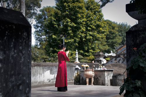 Free An Asian woman in a red dress prays at an outdoor shrine surrounded by greenery. Stock Photo