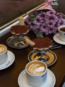 Charming setup with cappuccinos, tiramisu, and flowers for a cozy and delightful dining experience.
