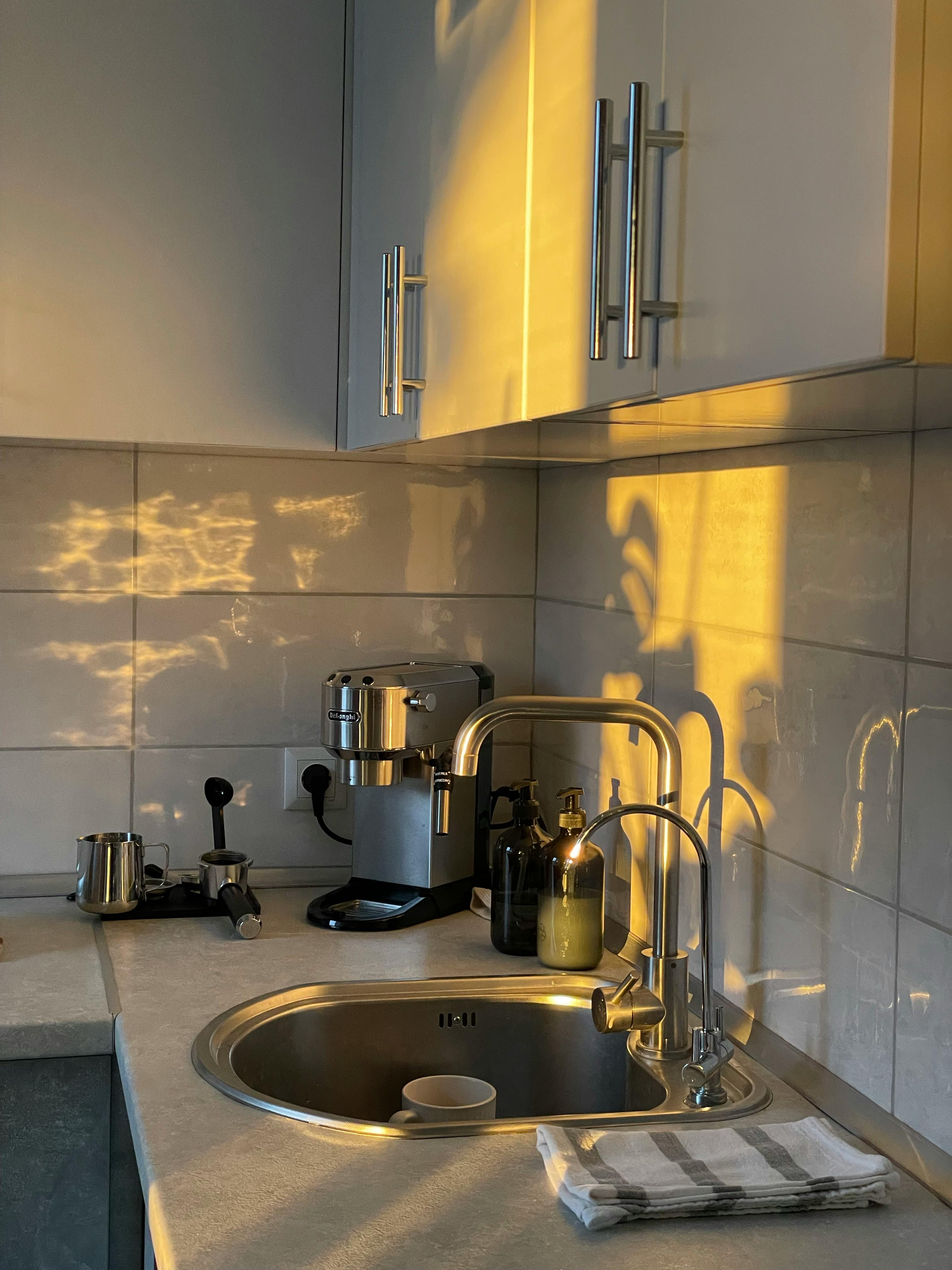 A cozy, modern kitchen corner with beautiful sunlight, featuring a coffee maker and sink.