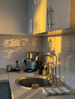 A cozy, modern kitchen corner with beautiful sunlight, featuring a coffee maker and sink.
