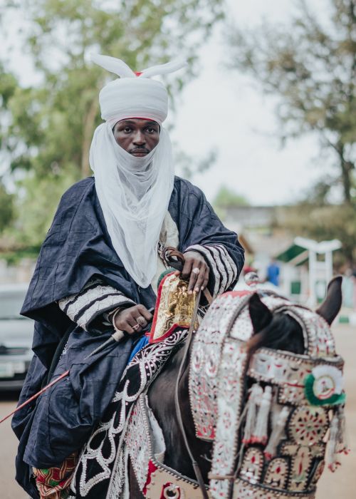 Free African man in traditional attire on a beautifully adorned horse, outdoors. Stock Photo