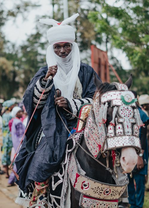 Free A traditional horseman wearing ornate garments rides a decorated horse during a cultural festival. Stock Photo