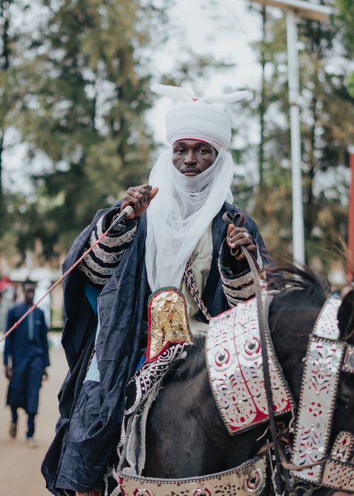 Free Man in traditional attire riding a decorated horse during a cultural parade. Stock Photo
