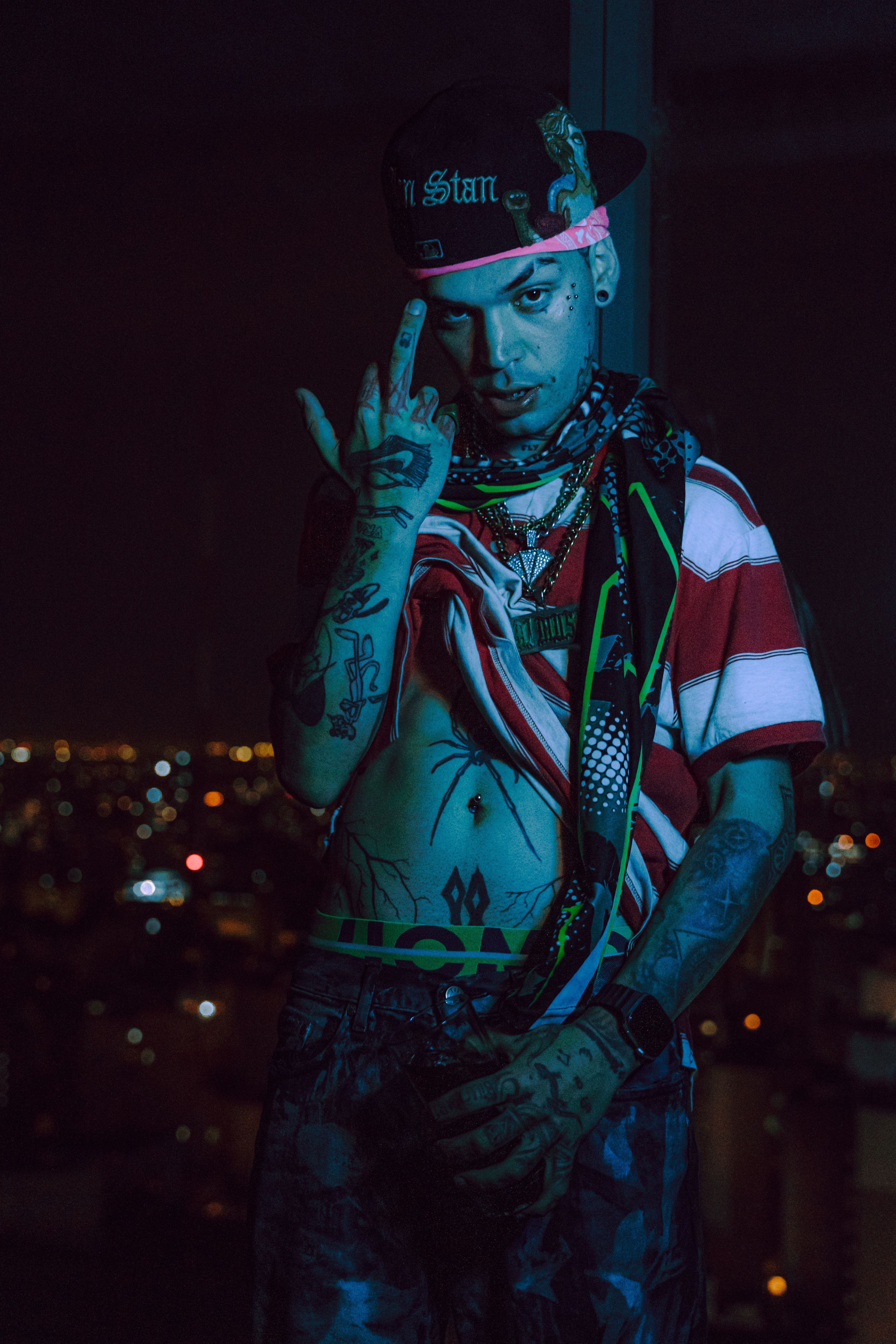 A tattooed performer poses confidently in an urban setting with city lights as a backdrop.