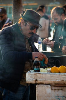 Photo by Faruk Boz A man prepares food at an outdoor market stall, adding spices to a dish with fresh lemons.