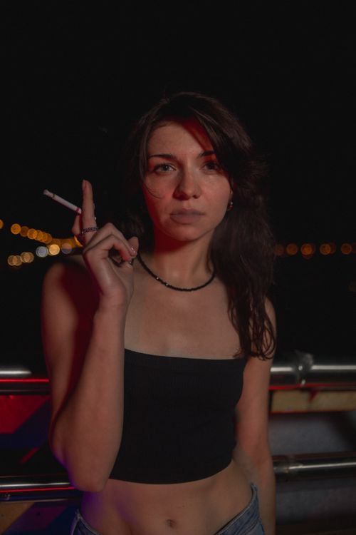 Free Portrait of a young woman smoking at night in Minsk, Belarus, with urban lights in the background. Stock Photo