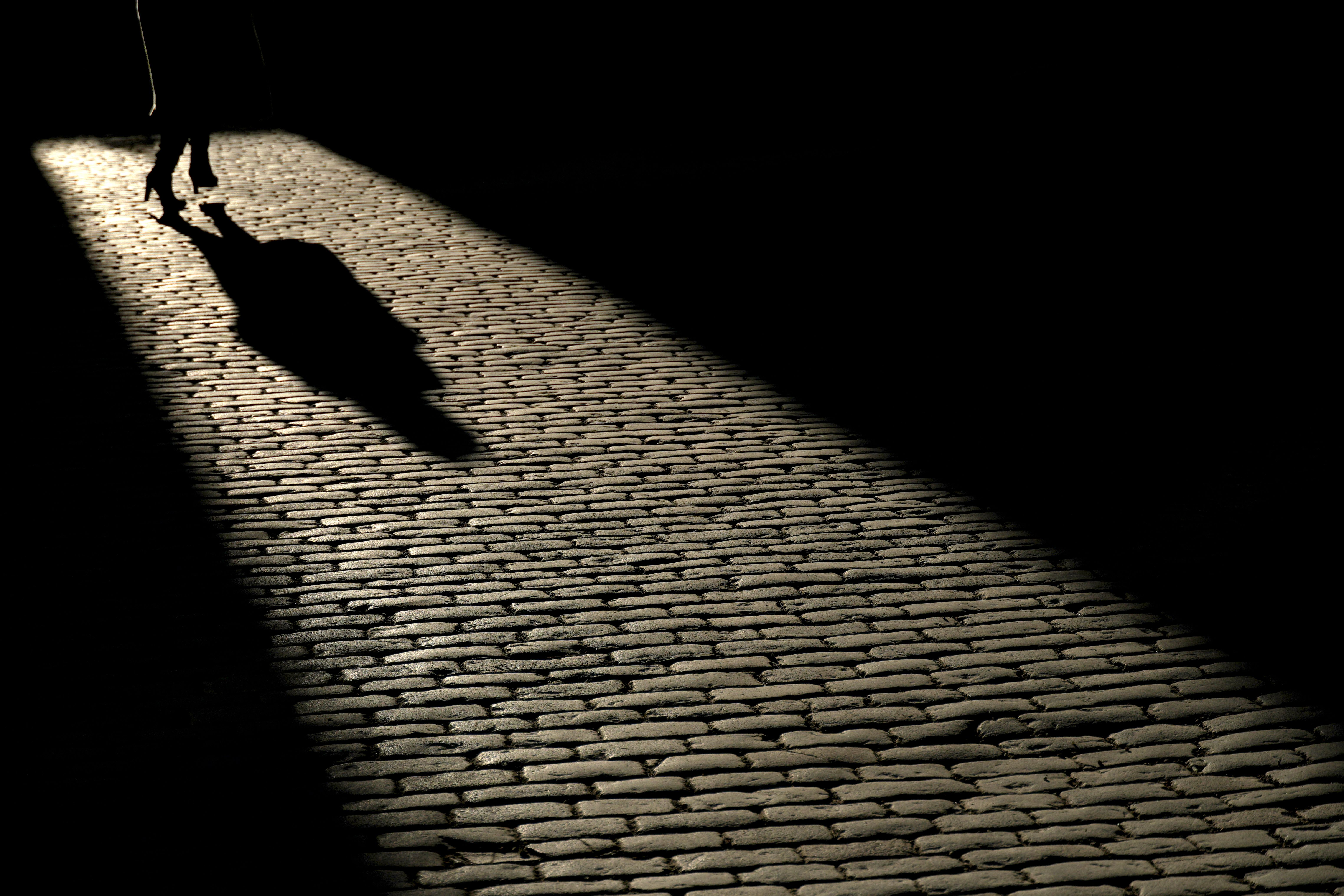 Silhouette of a person walking on a cobblestone street in Stockholm under a dramatic light.