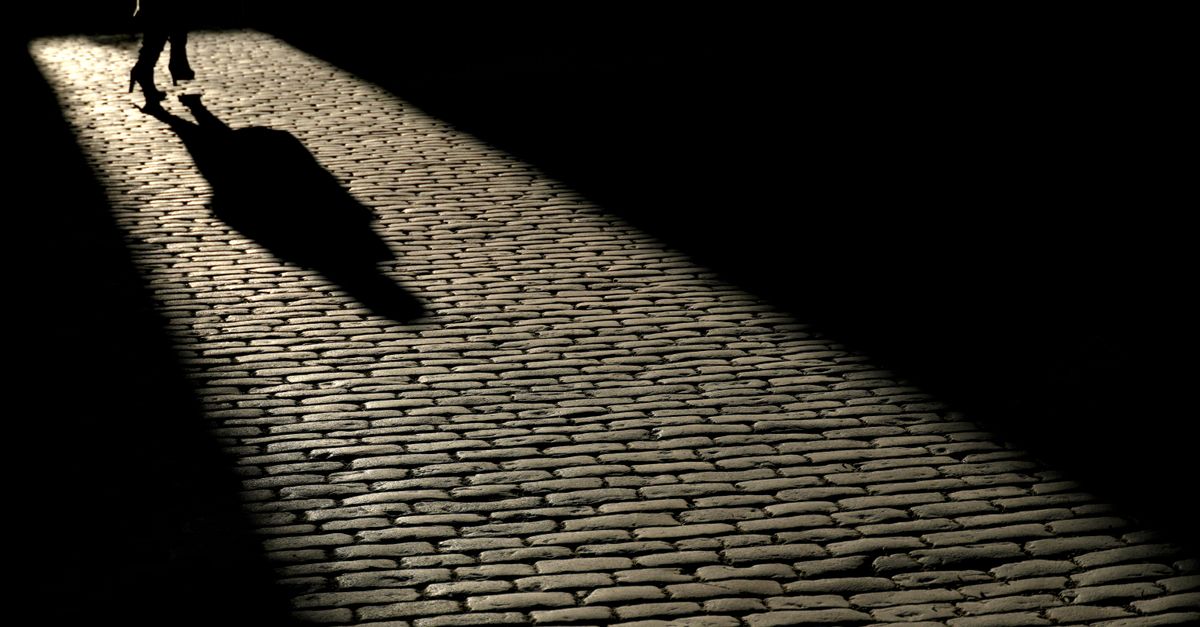 Silhouette of a person walking on a cobblestone street in Stockholm under a dramatic light.