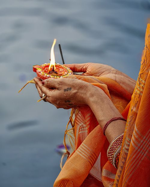 Free A close-up of hands performing a traditional ritual with a candle on a riverbank. Stock Photo
