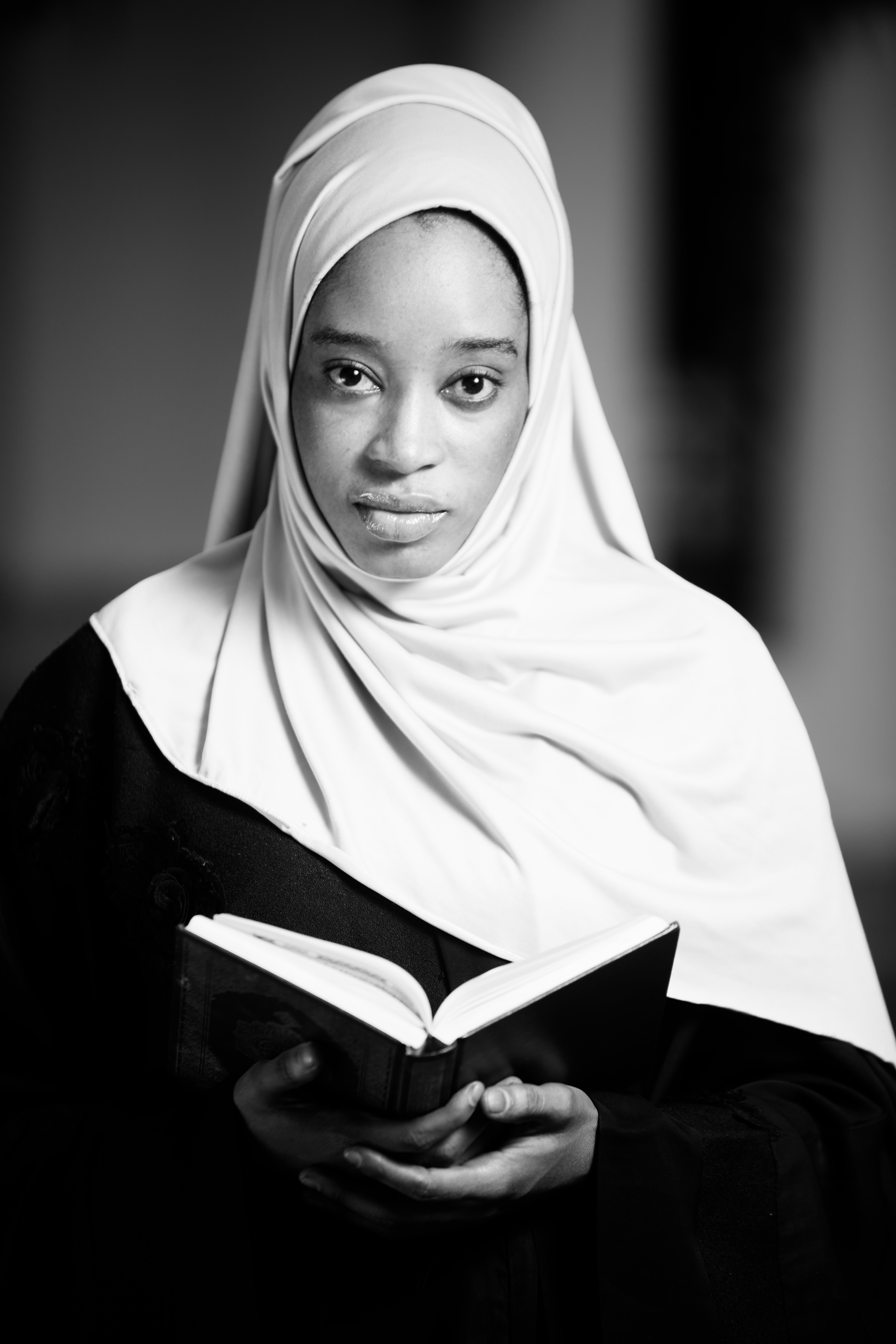 Black and white portrait of a young woman wearing a hijab holding a book.