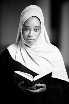 Black and white portrait of a young woman wearing a hijab holding a book.