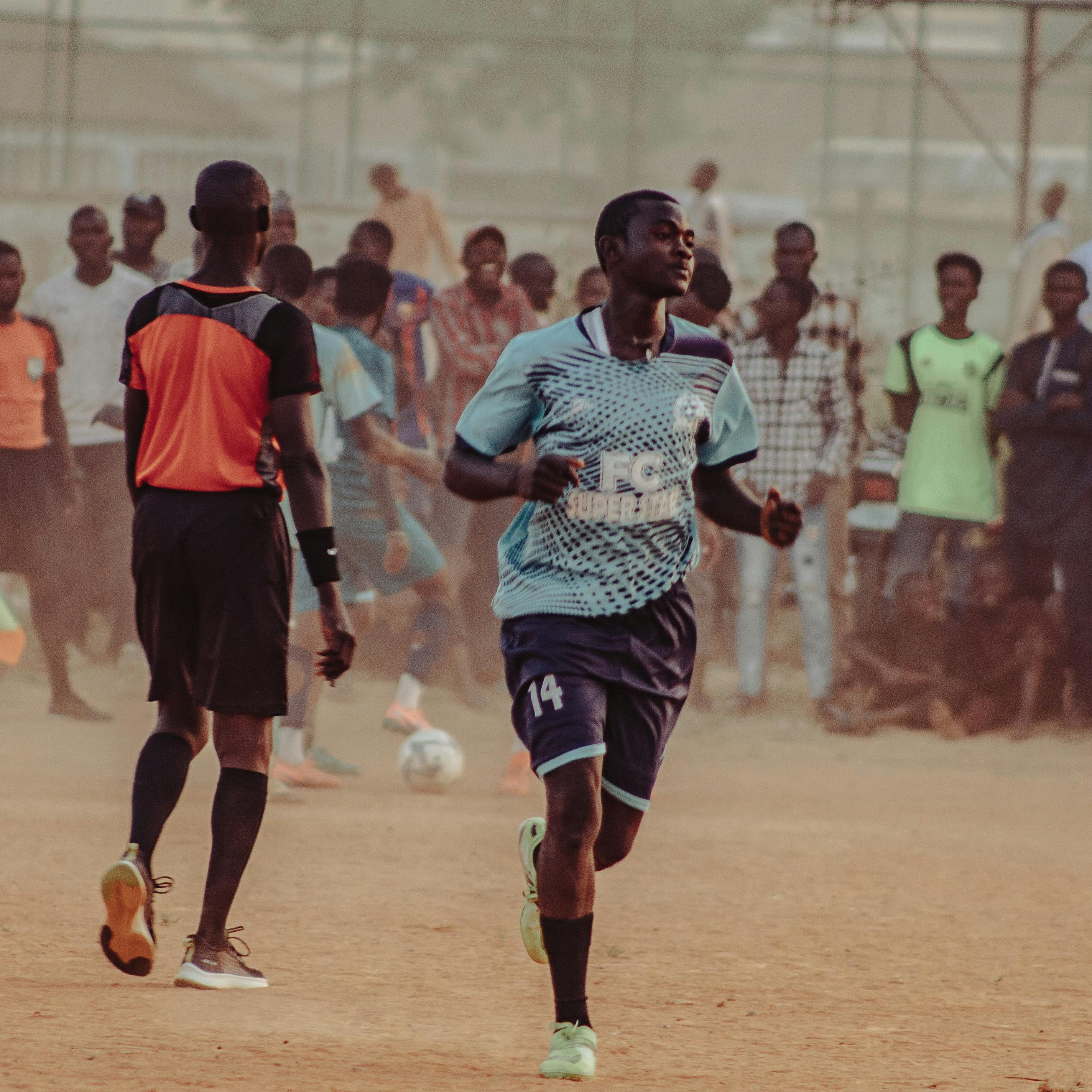 Dynamic local soccer match on a dusty outdoor field with players and referee in action.