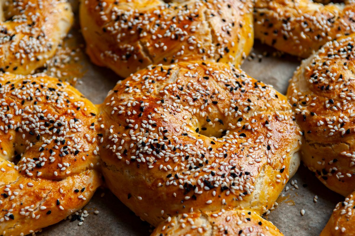 Egg-glazed twisted bread rings covered in white sesame and black nigella seeds on parchment