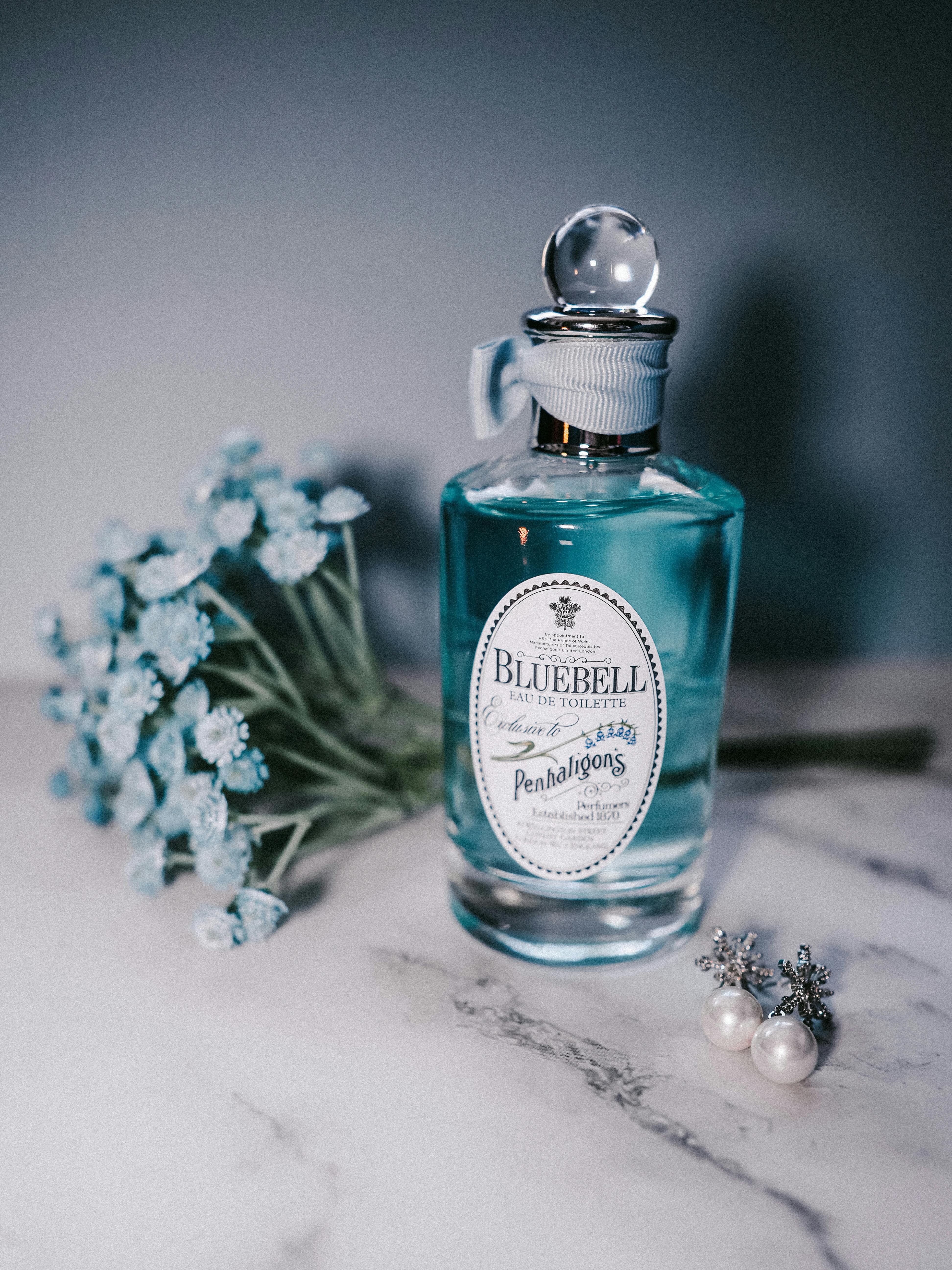A luxury blue perfume bottle with flowers and elegant earrings on marble surface.