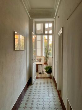 Sunlit hallway with open door revealing plants and tiled floor.