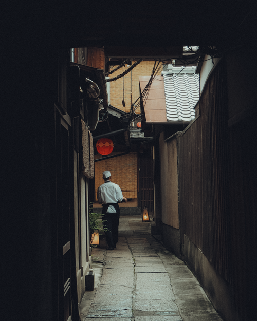 Free Chef walks in Kyoto alley with lanterns and traditional architecture. Moody ambiance. Stock Photo