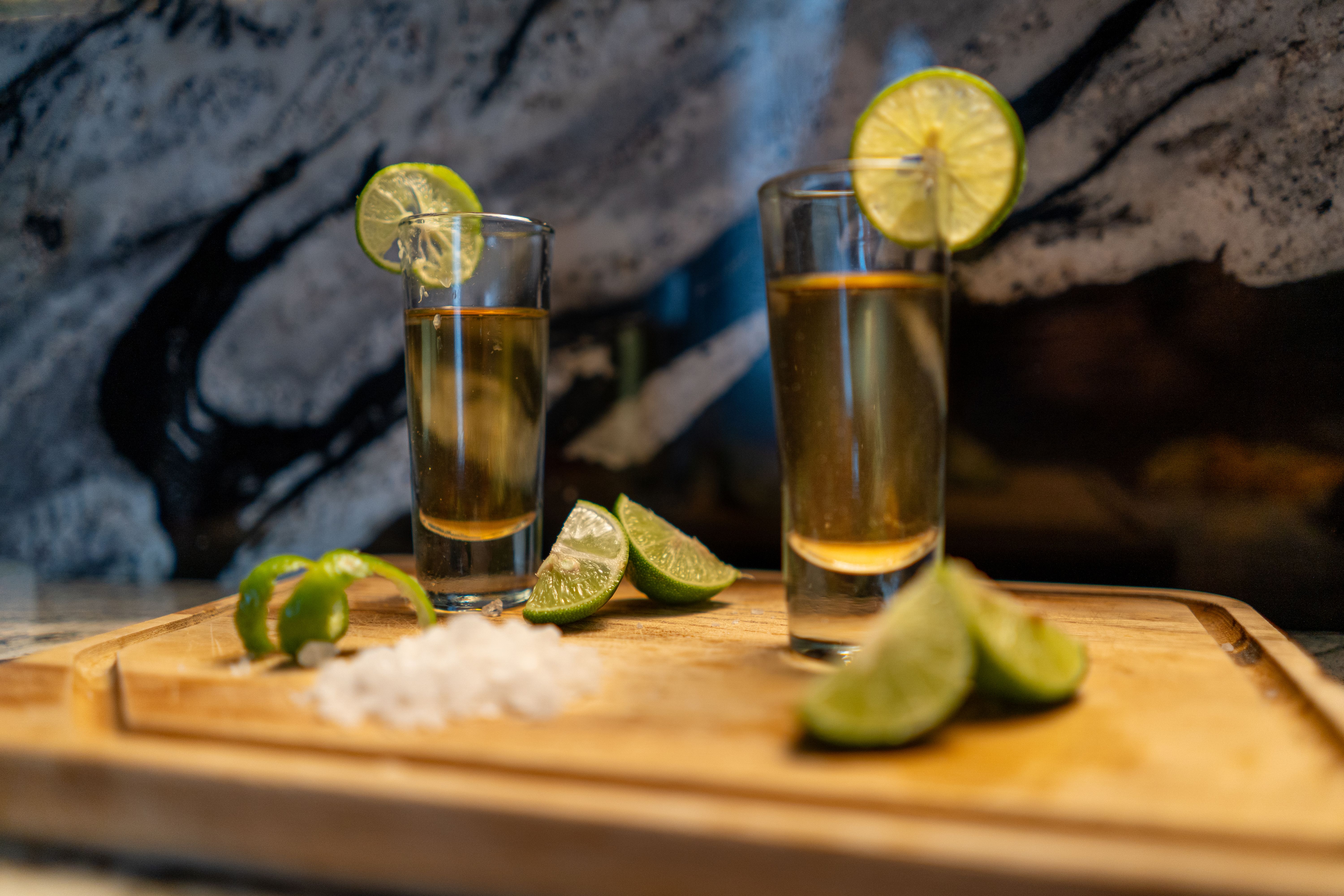 Two tequila shots with lime wedges on a wooden board, complemented by a rustic background.