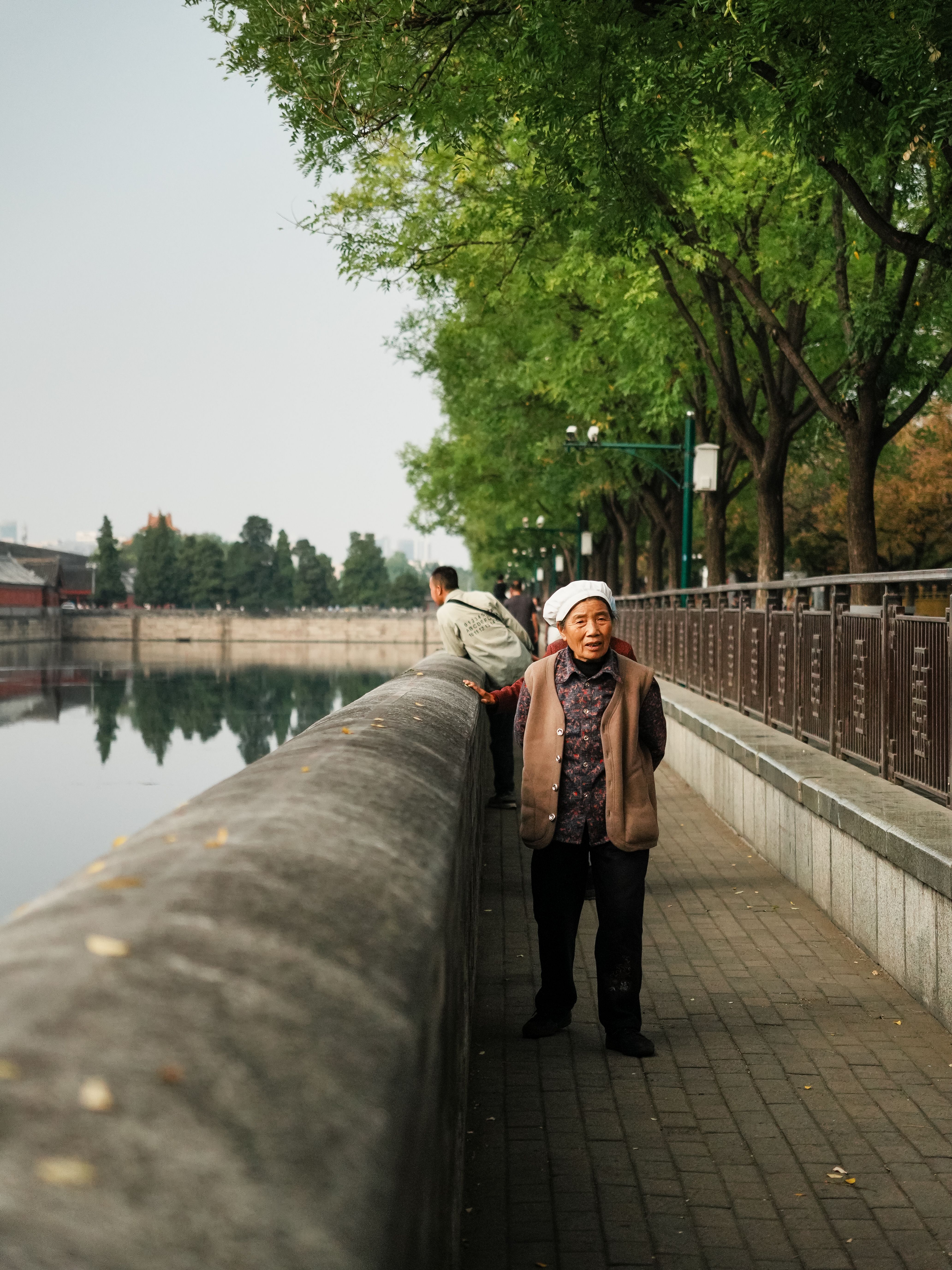 Elderly Woman Strolling by Urban Riverside Walkway · Free Stock Photo