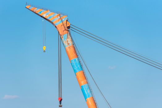 A vibrant orange and blue crane extending into a bright clear sky, displaying industrial strength and color.